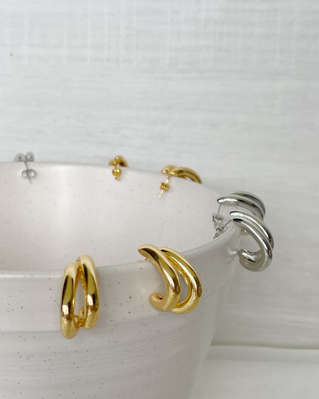 Gold hoop earrings displayed on a white ceramic dish with a white background
