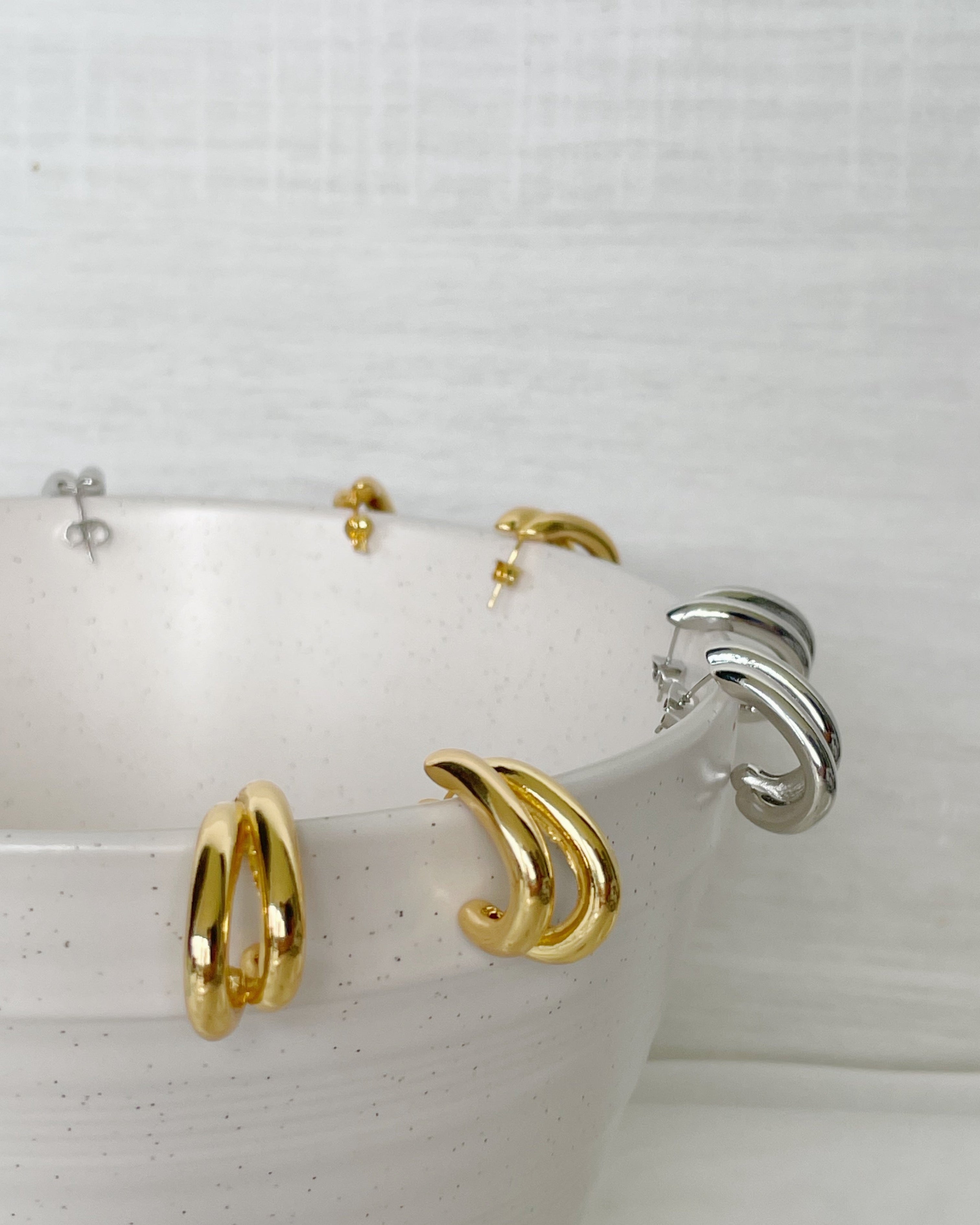 Gold hoop earrings displayed on a white ceramic dish with a white background