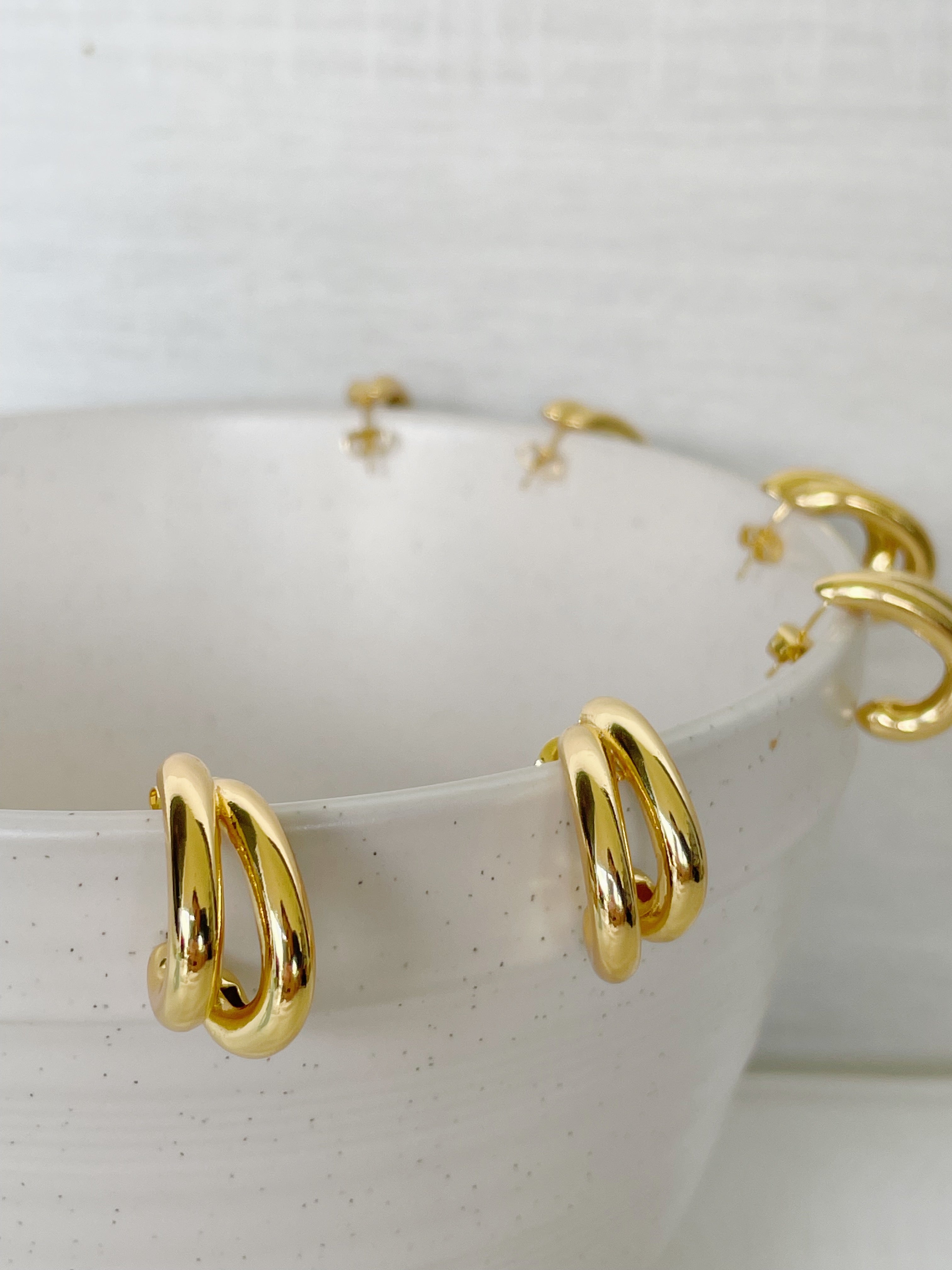 Gold hoop earrings on a white ceramic dish with a speckled pattern
