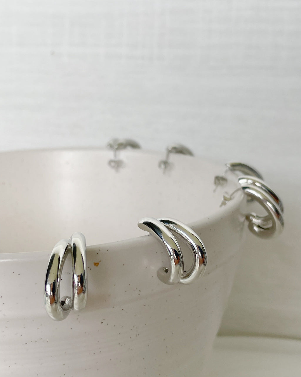 Silver hoop earrings displayed on a white ceramic dish.