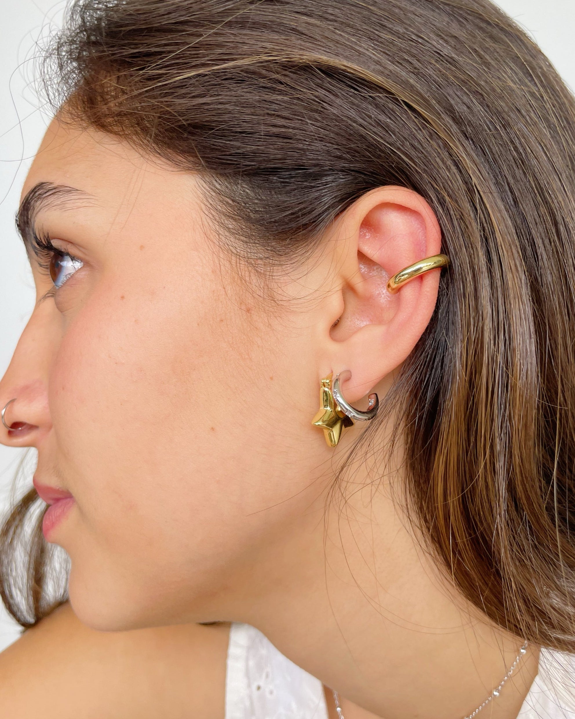 Close-up of a person wearing gold hoop earrings with a plain background